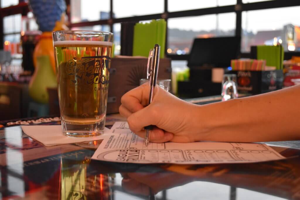 Hand writing on trivia answer sheet next to pint of beer