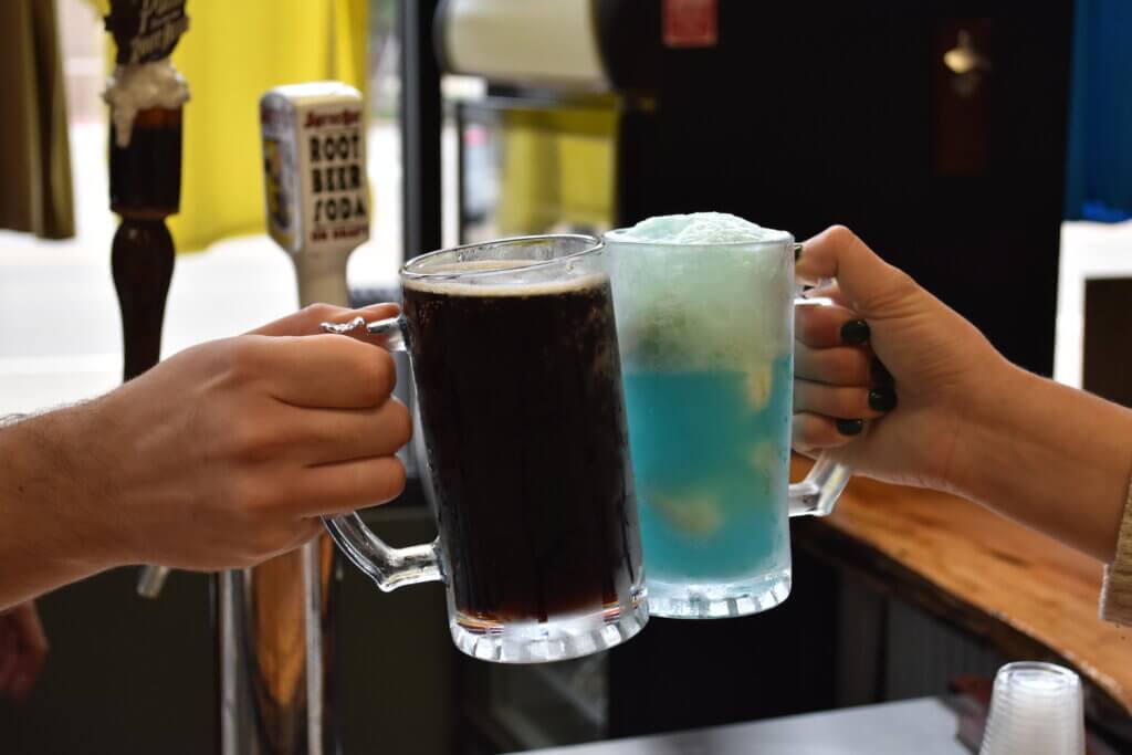 Mug of root beer and blue soda float clinking in a "cheers"