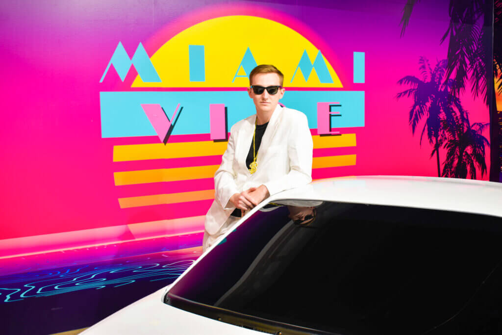 Man in white suit posing with white Ferrari with Miami Vice backdrop