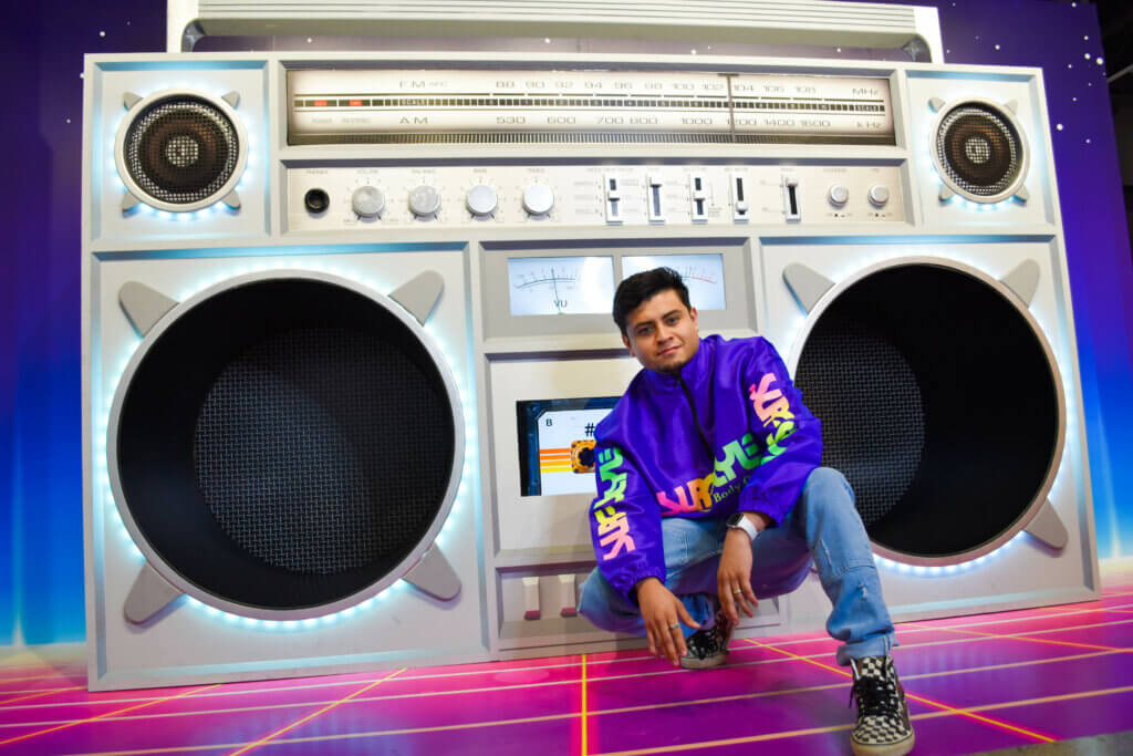 Man in purple windbreaker posing in front of larger-than-life boombox