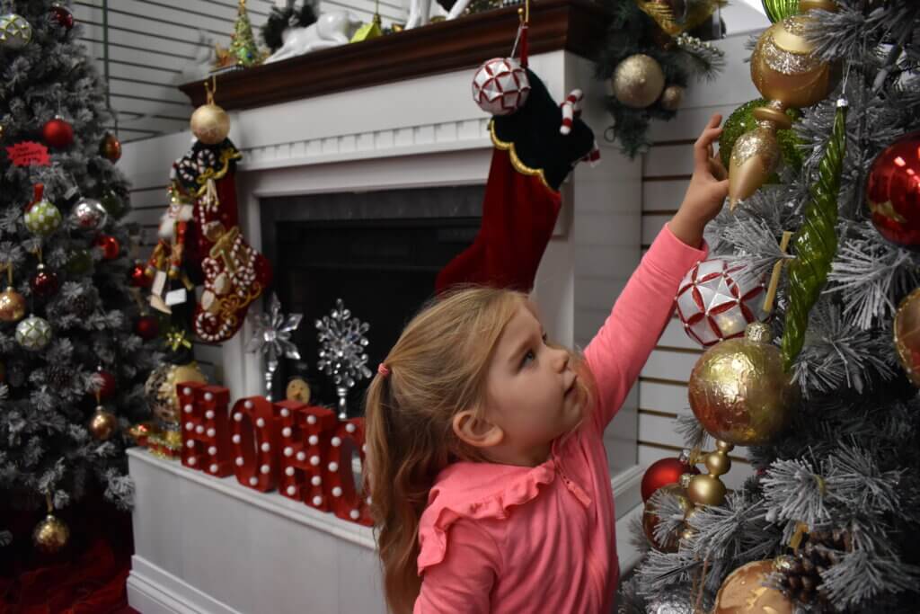 Young girl reaching for ornament on Christmas Tree at Forever Christmas shop