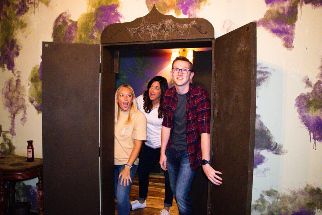 Two women and one man walking into an escape room with faces of wonder and surprise