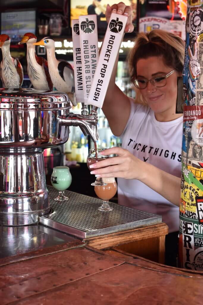 Woman pouring bright colored beers behind the bar