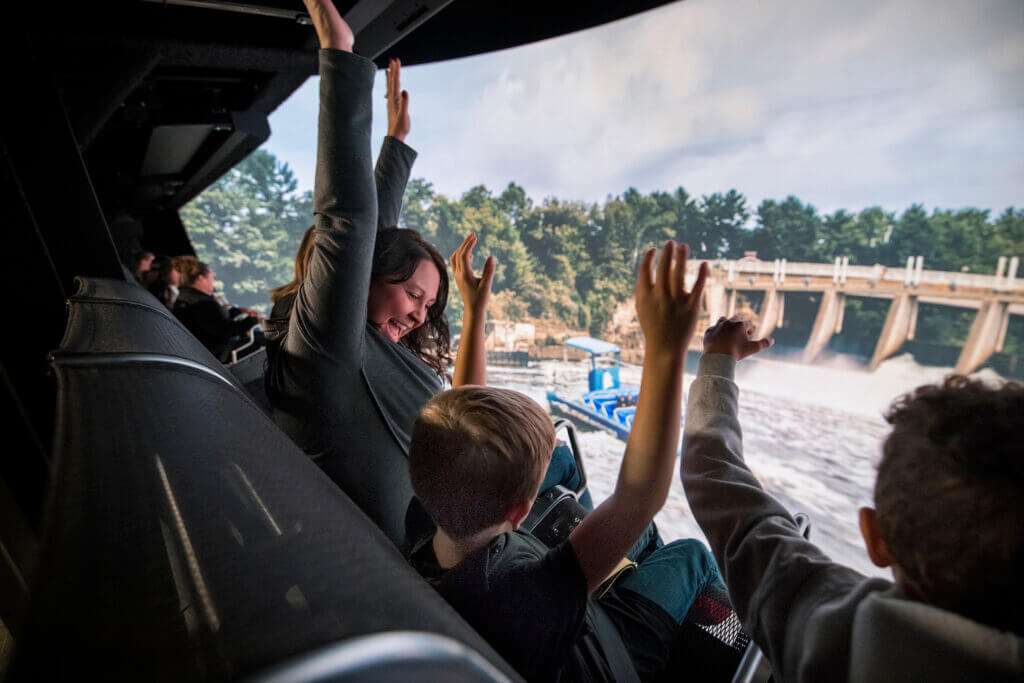 Mom and children with their hands up in front of Take Flight's giant screen